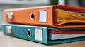 A stack of orange and teal binders filled with documents sits on a wooden surface. Royalty Free Stock Photo