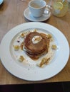 Stack of pancakes covered in maple syrup, sprinkled with nuts, pieces of banana with whipped cream. On a plate in a restaurant