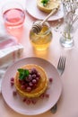 Stack of pancakes with frozen raspberry, red currant and honey on pink background. Selective focus