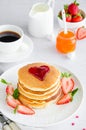 A stack of pancakes with a heart of jam on top with fresh strawberries and mint on a white plate on a light background. Royalty Free Stock Photo