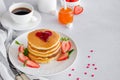 A stack of pancakes with a heart of jam on top with fresh strawberries and mint on a white plate on a light background. Royalty Free Stock Photo