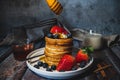 A stack of pancakes with pouring honey, fresh blueberry and strawberry and whip cream on top in plate on wooden table