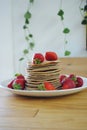 Stack of pancakes with some organic and fresh strawberries. Some green plants on the background. Sweet and tasty food concept