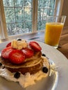Stack of pancakes with strawberries, blueberries, bananas, and cream with juice Royalty Free Stock Photo
