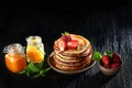 A stack of pancakes with strawberries and mint . Jars of honey on the table. Photo on a black background. Copy of the space. The Royalty Free Stock Photo