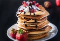 Stack of pancakes with strawberries, whip cream and chocolate syrup on a white plate on a black background. Royalty Free Stock Photo