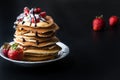 Stack of pancakes with strawberries, whip cream and chocolate syrup on a white plate on a black background. Royalty Free Stock Photo