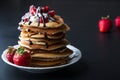 Stack of pancakes with strawberries, whip cream and chocolate syrup on a white plate on a black background. Royalty Free Stock Photo