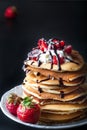 Stack of pancakes with strawberries, whip cream and chocolate syrup on a white plate on a black background. Royalty Free Stock Photo