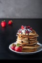 Stack of pancakes with strawberries, whip cream and chocolate syrup on a white plate on a black background. Royalty Free Stock Photo