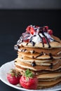 Stack of pancakes with strawberries, whip cream and chocolate syrup on a white plate on a black background. Royalty Free Stock Photo