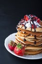 Stack of pancakes with strawberries, whip cream and chocolate syrup on a white plate on a black background. Royalty Free Stock Photo