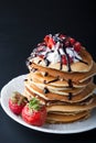 Stack of pancakes with strawberries, whip cream and chocolate syrup on a white plate on a black background. Royalty Free Stock Photo