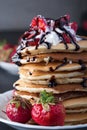 Stack of pancakes with strawberries, whip cream and chocolate syrup on a white plate on a black wooden background. Royalty Free Stock Photo