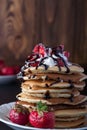 Stack of pancakes with strawberries, whip cream and chocolate syrup on a white plate on a black wooden background. Royalty Free Stock Photo