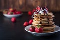 Stack of pancakes with strawberries, whip cream and chocolate syrup on a white plate on a black wooden background. Royalty Free Stock Photo