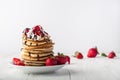 Stack of pancakes with strawberries, whip cream and chocolate syrup on a white plate on a white wooden background. Royalty Free Stock Photo