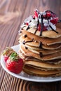 Stack of pancakes with strawberries, whip cream and chocolate syrup on a white plate on a wooden background. Royalty Free Stock Photo