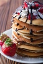 Stack of pancakes with strawberries, whip cream and chocolate syrup on a white plate on a wooden background. Royalty Free Stock Photo