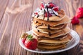 Stack of pancakes with strawberries, whip cream and chocolate syrup on a white plate on a wooden background. Royalty Free Stock Photo