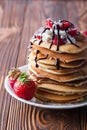 Stack of pancakes with strawberries, whip cream and chocolate syrup on a white plate on a wooden background. Royalty Free Stock Photo