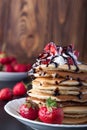 Stack of pancakes with strawberries, whip cream and chocolate syrup on a white plate on a wooden background. Royalty Free Stock Photo