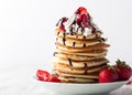 Stack of pancakes with strawberries, whip cream and chocolate syrup on a white wooden plate on a white woode background. Royalty Free Stock Photo