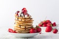 Stack of pancakes with strawberries, whip cream and chocolate syrup on a white wooden plate on a white woode background. Royalty Free Stock Photo