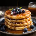 A stack pancakes topped with fresh blueberries and drizzled with syrup on background