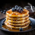 A stack pancakes topped with fresh blueberries and drizzled with syrup on background