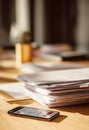 stack of paper documents and smartphone on wooden office desk in bright sunlight, professional workspace with business files and Royalty Free Stock Photo