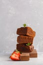 Stack of pieces of homemade dark chocolate brownie with strawberries on a wooden board, copy space.