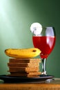 Stack or pile of crackers, a banana and a goblet of fruit juice with cucumber slices