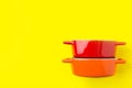 Stack of red and orange ceramic cocottes on bright yellow background. Cooking baking cookware concept. Workshop poster banner