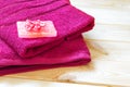 Stack of red terry towels and piece of rose soap with fabric flower on it, lied on wooden table