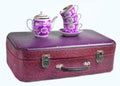 A stack of retro cups and a ceramic teapot on old leather suitcase isolated on a white background. Royalty Free Stock Photo