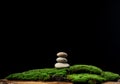 Stack of round stones on green moss, black background. Podium to showcase products, cosmetics and items, advertising