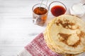 Stack of Russian pancakes on a plate, a mug of black tea, jam, sour cream, sauce, on a towel with a red pattern on a white Royalty Free Stock Photo