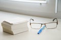 Stack of sheets for notes, glasses and a pen lie on the windowsill in the office. Work on cataloging