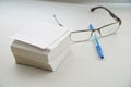 A stack of sheets for records, glasses and a fountain pen are on a white table by the window in the office. Work on cataloging