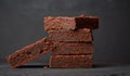 Stack of square baked pieces of brownie chocolate cake on a black background