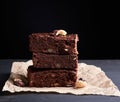 Stack of square baked slices of brownie chocolate cake with walnuts on a wooden surface. Cooked homemade food