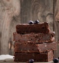 Stack of square baked slices of brownie chocolate cake with walnuts on a wooden surface. Cooked homemade food