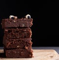 Stack of square baked slices of brownie chocolate cake with walnuts on a wooden surface