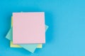 Stack of sticky notes on solid blue background with yellow, blue and pink on top with copy space for writing message using as memo