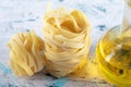 Stack of tagliatelle nests and glass of olive oil on blue background