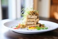 stack of tempeh slices on white plate, soybeans at side