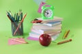 Stack of textbooks, alarm clock, apple and school supplies, green background, back to school concept Royalty Free Stock Photo