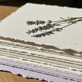 A stack of textured, beige handmade paper with deckled edges lies on a wooden Royalty Free Stock Photo
