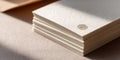 Stack of textured cream-colored paper sheets with embossed circular logo detail on top, arranged neatly on a soft beige surface in Royalty Free Stock Photo
